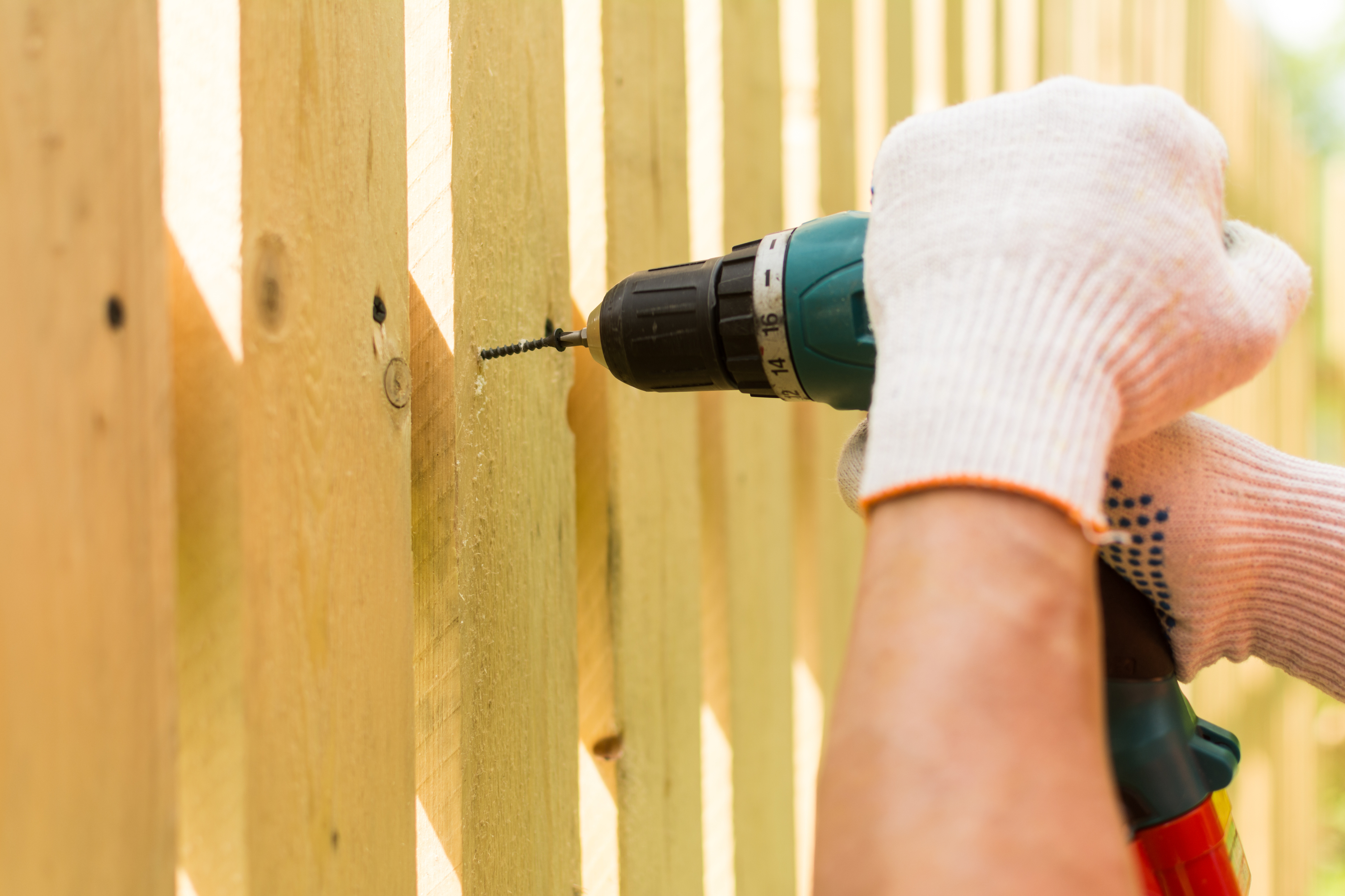 Close-up of person wearing glove drilling into a wooden fence