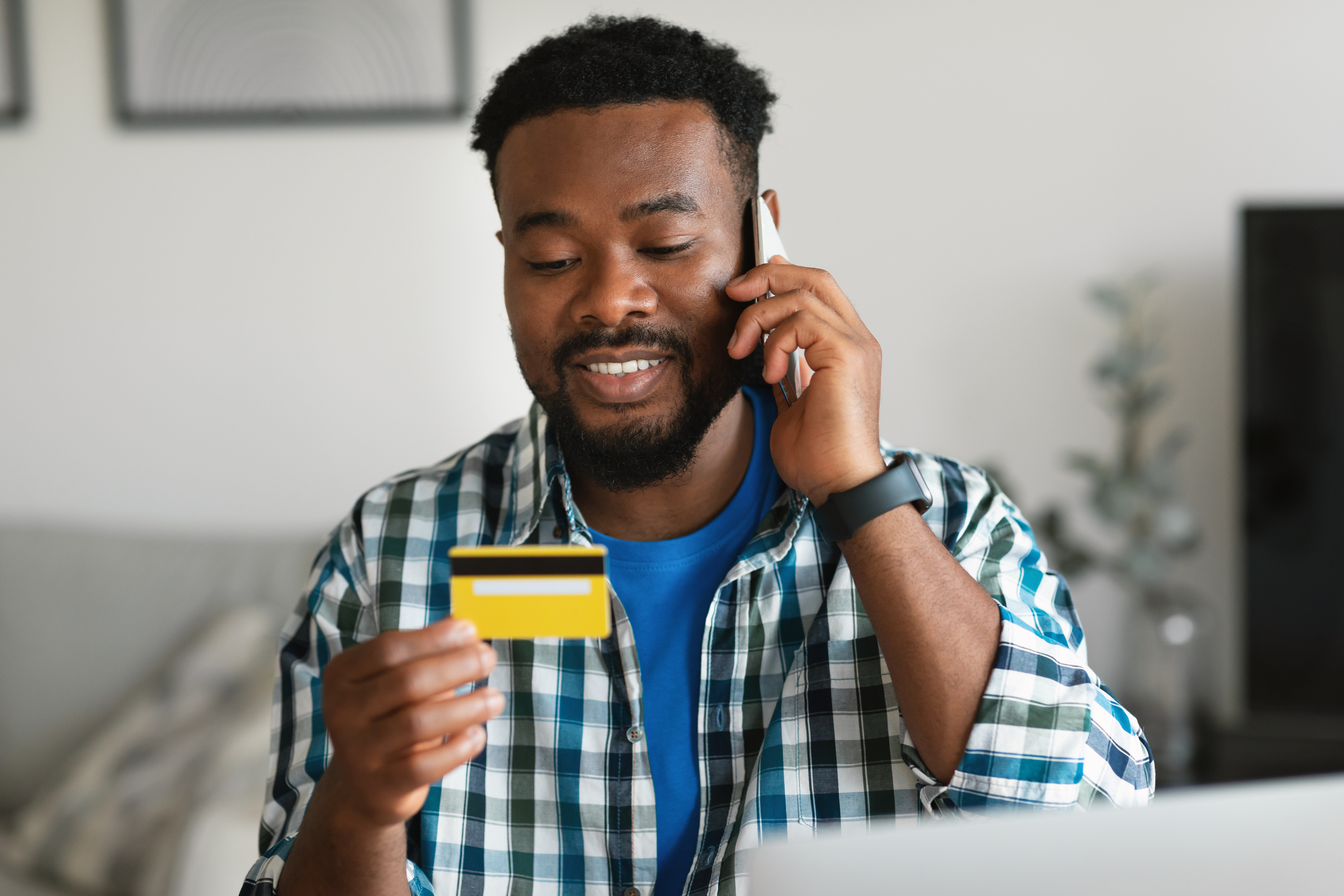 Man with phone to his ear in one hand, looking at the credit card he is holding in the other hand