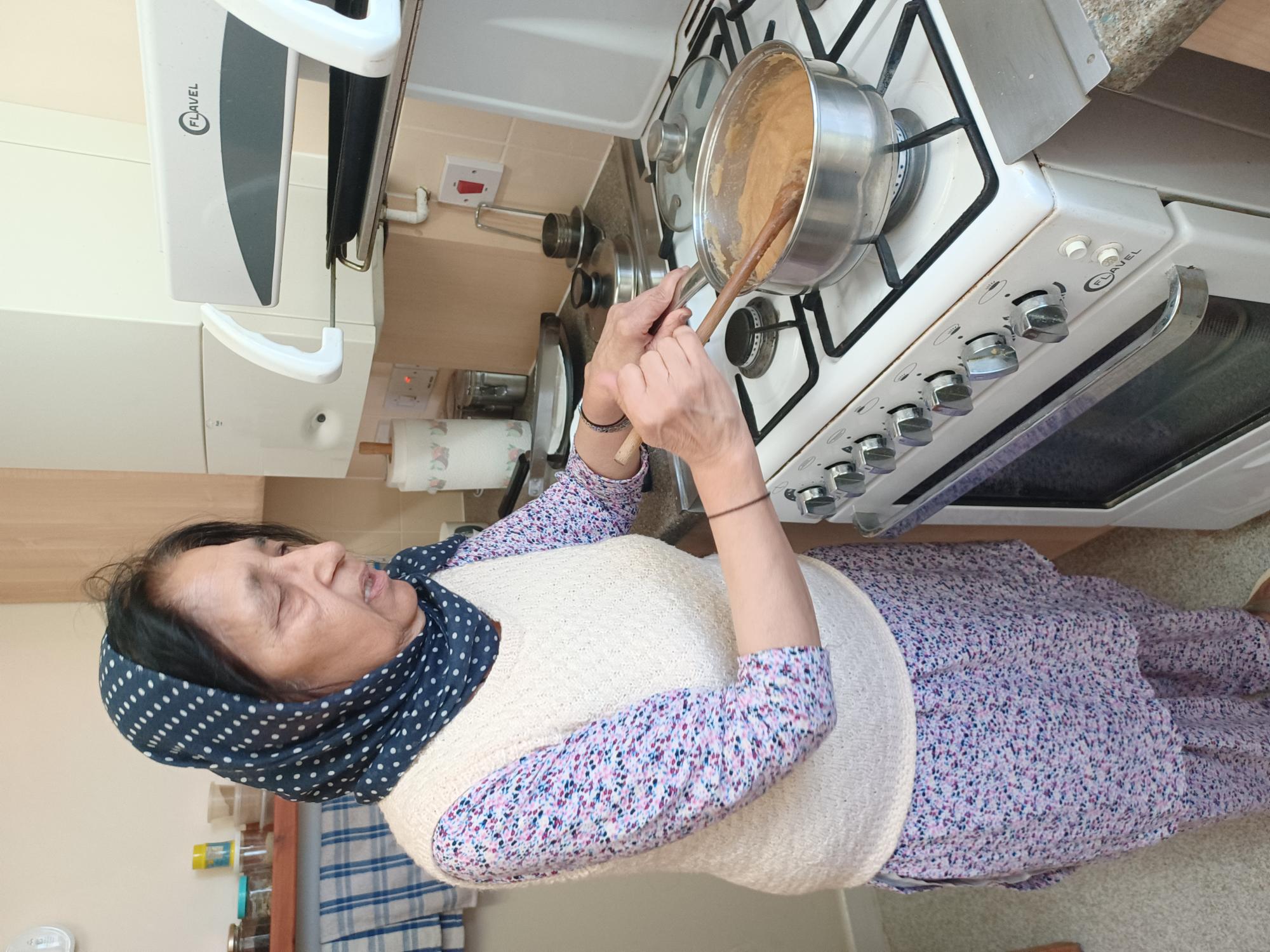 Lady stands at a cooker stirring a pan with semolina pudding in