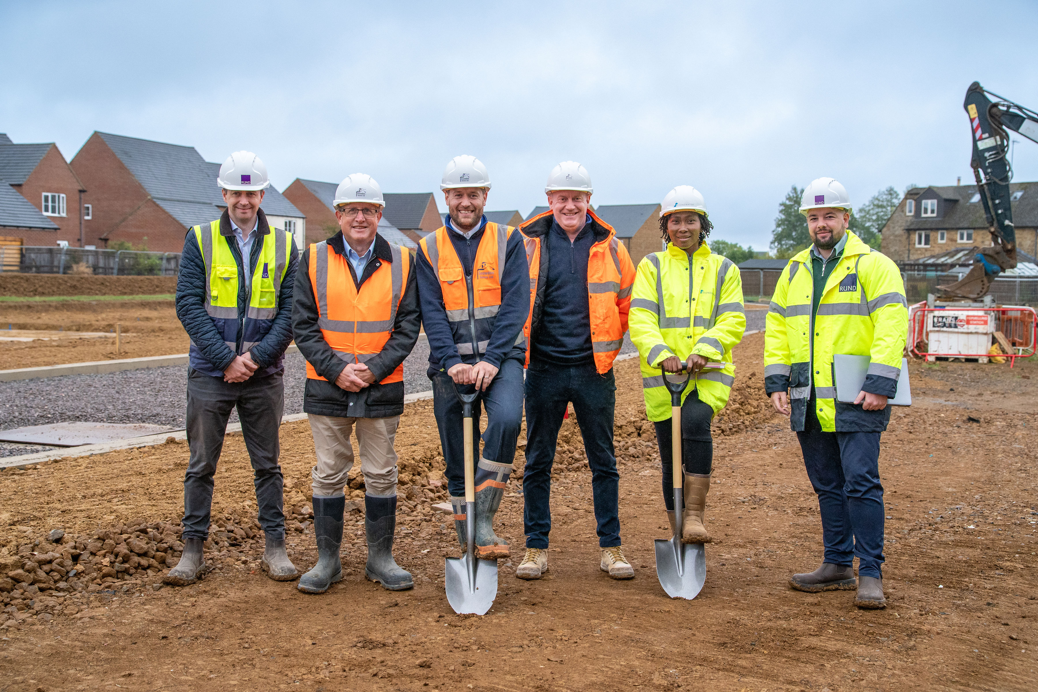A row of people in protective clothing, two with spades on a construction site