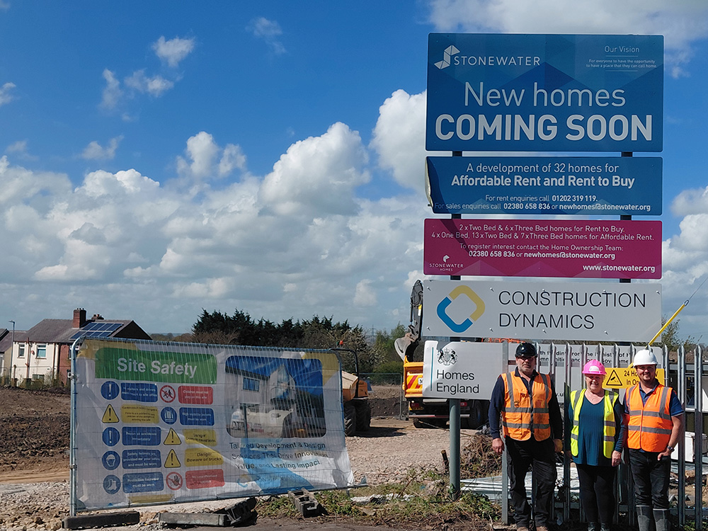 Three people stood outside in front of a Stonewater new homes sign