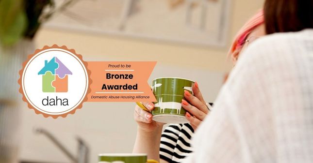 daha rosette with tail reads proud to be Bronze awarded, sits over lady holding a cup in soft focus