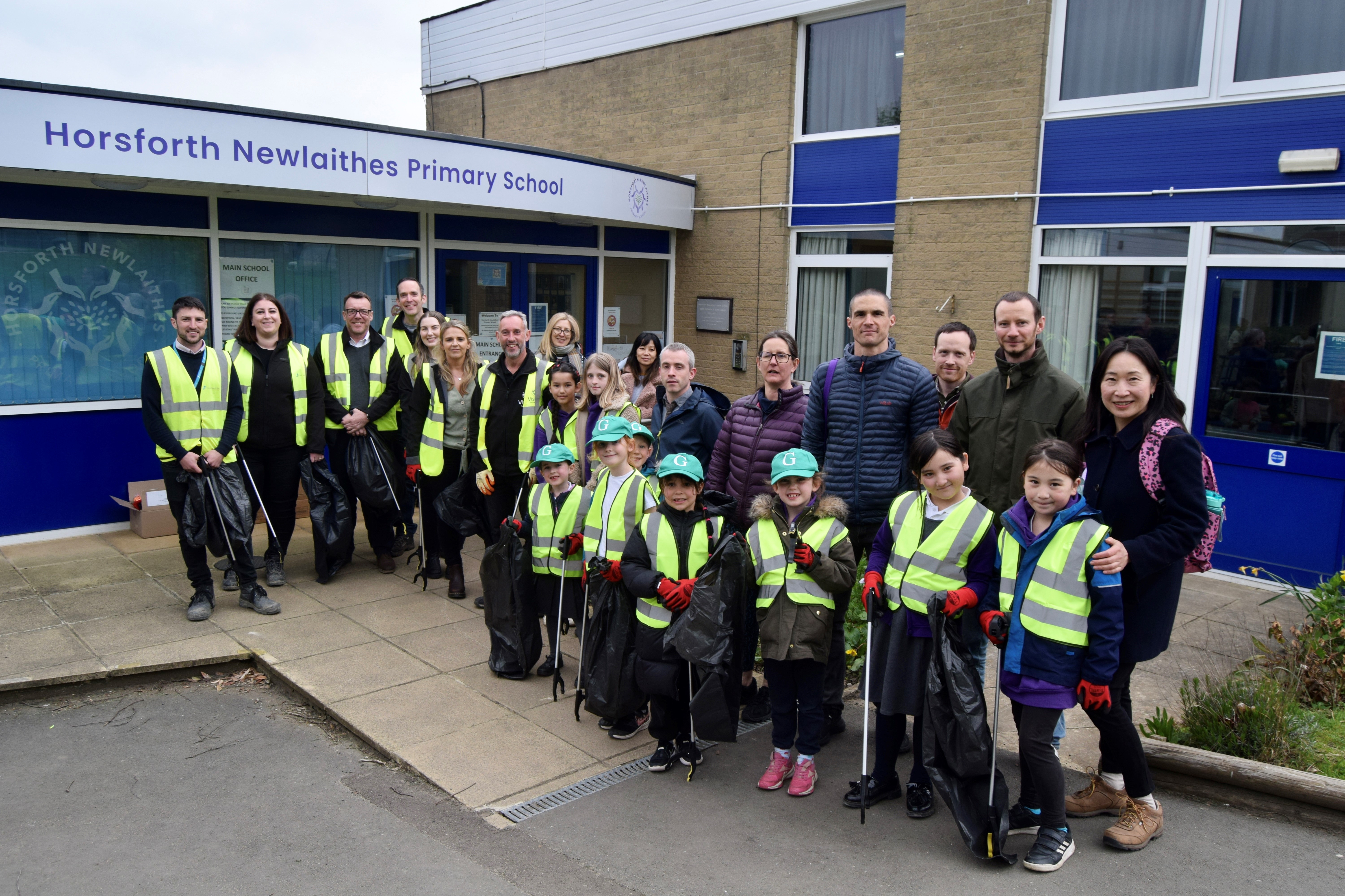 Group of Newlaithes school children and teachers with hi-vis jackets, holding litter pickers