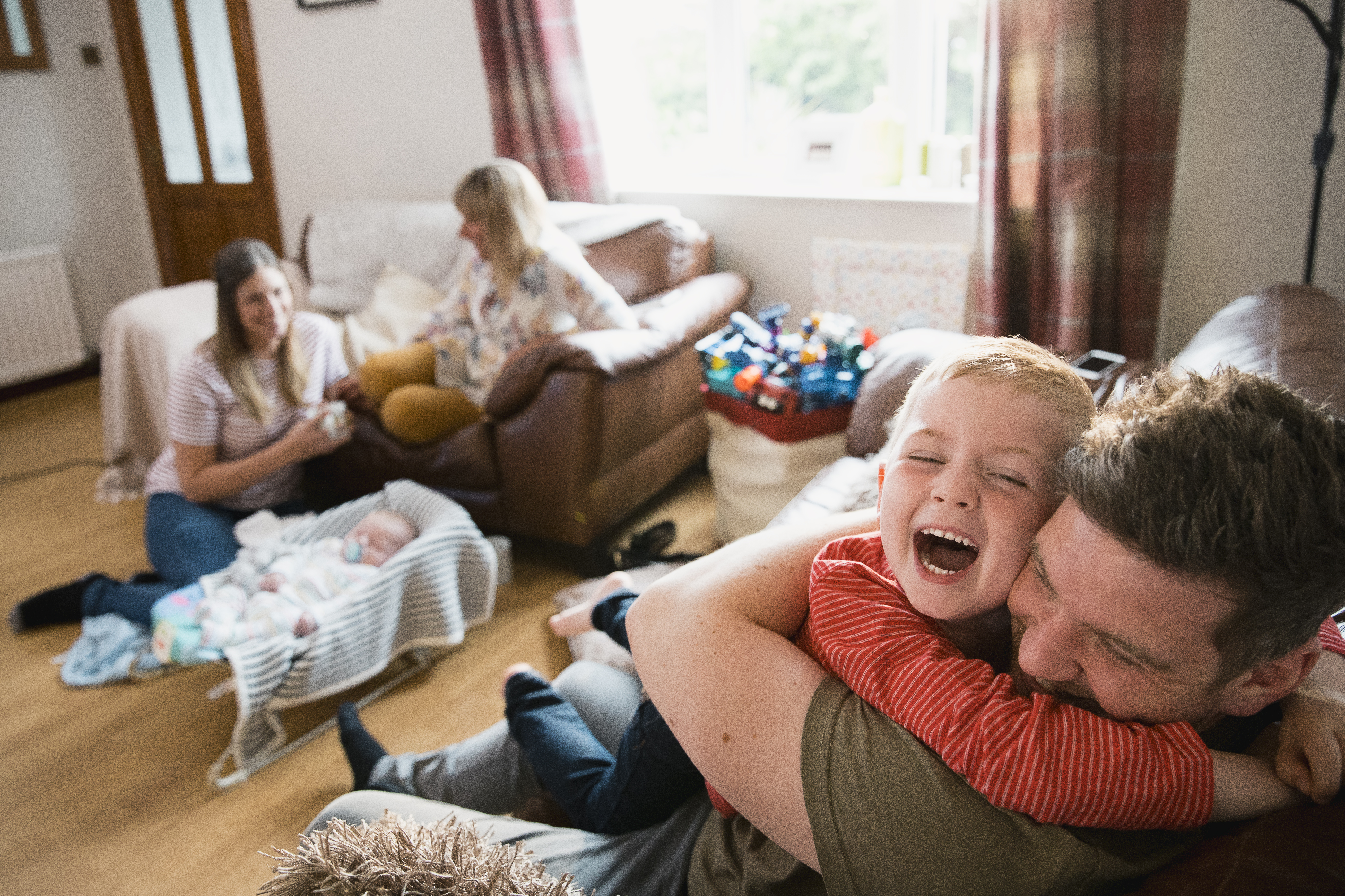 Living room scene of young boy smiling and hugging father with family sitting in the background