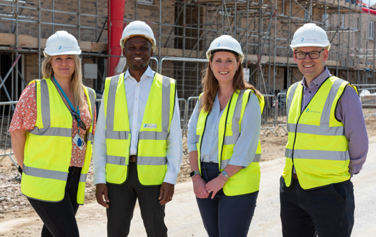 Four colleagues in hi-vis jackets and hard hats smiling and facing camera, stood at development site