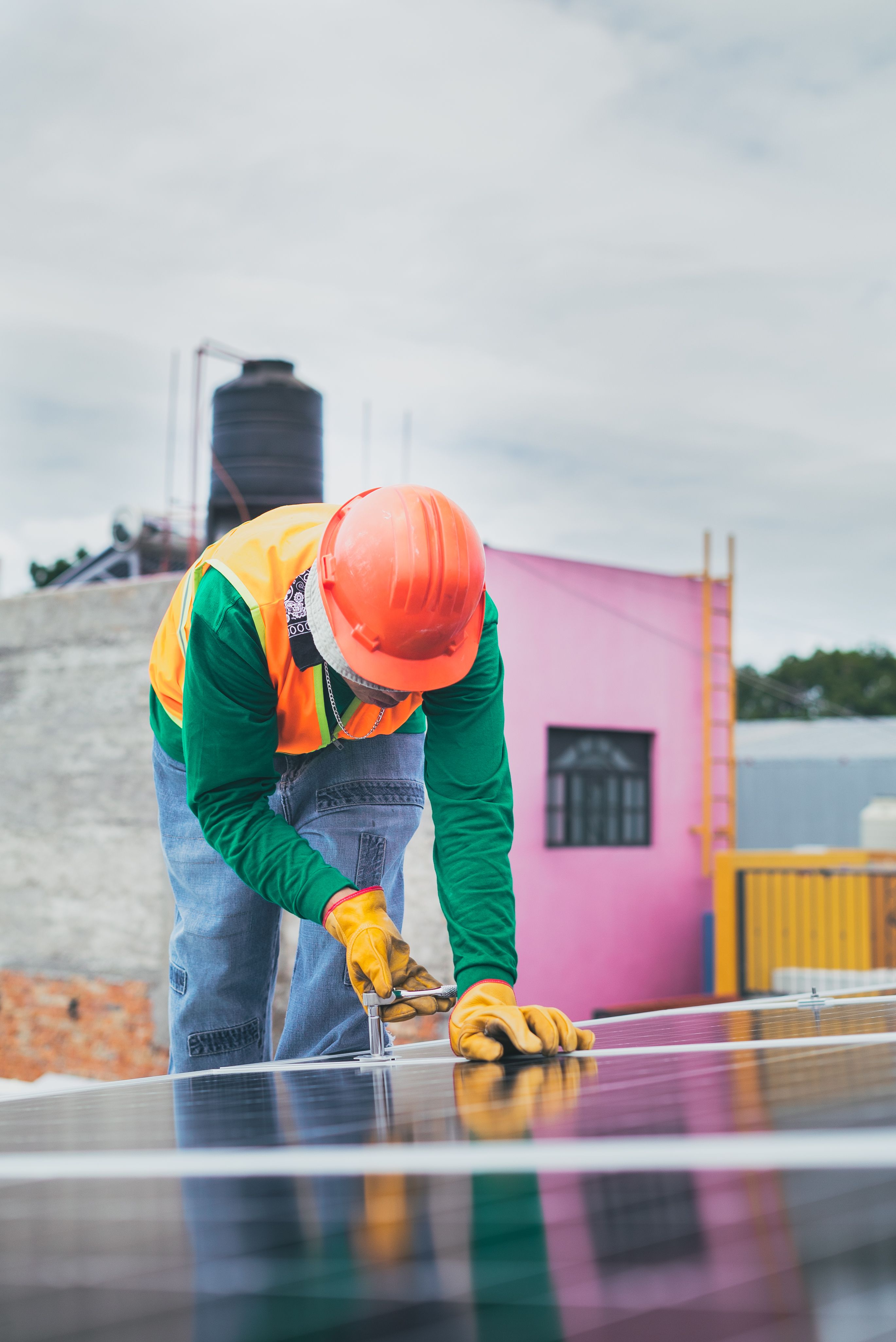 A person is leant over wearing PPE hat and gloves installing solar panels